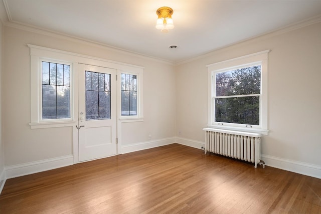 empty room featuring wood finished floors, baseboards, visible vents, radiator heating unit, and crown molding