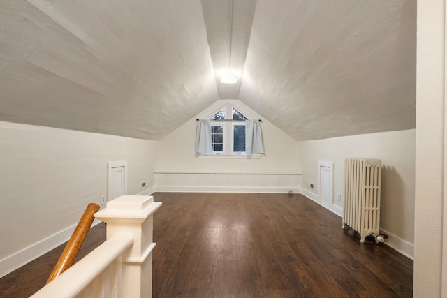 additional living space with dark wood-style floors, baseboards, radiator heating unit, and lofted ceiling