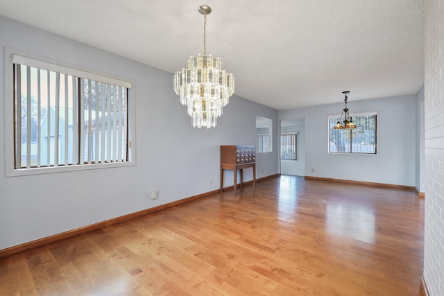 unfurnished room featuring a textured ceiling, light wood-style flooring, plenty of natural light, and a chandelier