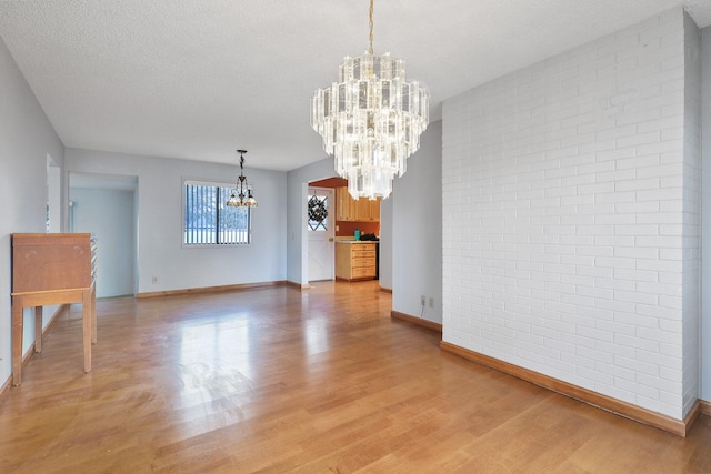 unfurnished dining area with an inviting chandelier, light wood-style flooring, baseboards, and a textured ceiling