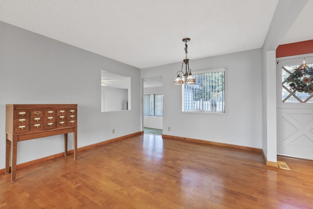 unfurnished dining area with a notable chandelier, wood finished floors, baseboards, and a textured ceiling