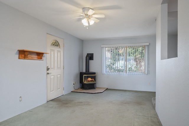 interior space with a wood stove, carpet floors, and ceiling fan