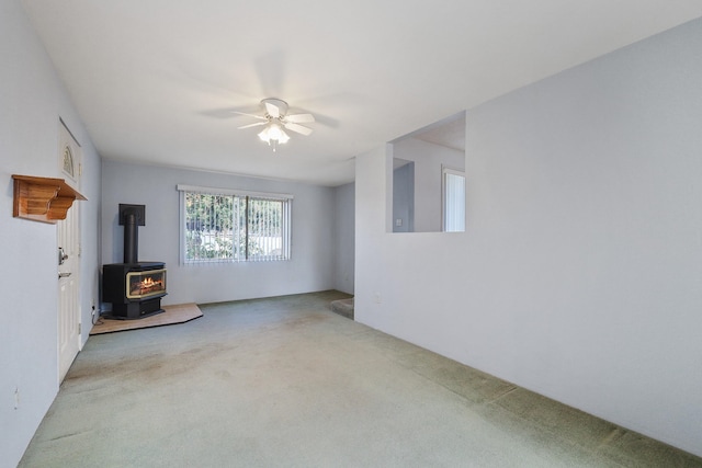 unfurnished living room featuring a wood stove, ceiling fan, and carpet floors