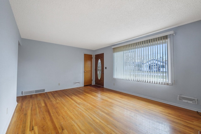 empty room with visible vents, a textured ceiling, baseboards, and hardwood / wood-style flooring