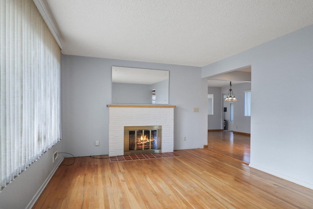 unfurnished living room featuring a brick fireplace, a textured ceiling, an inviting chandelier, and wood finished floors