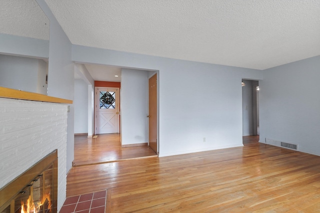 unfurnished living room with visible vents, a fireplace, a textured ceiling, and wood finished floors