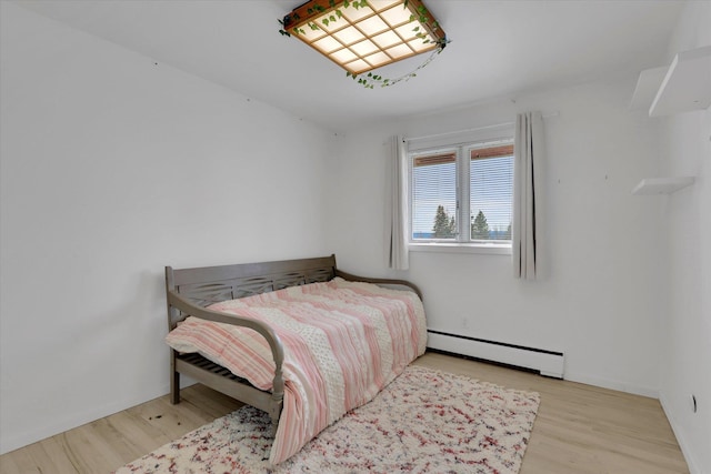 bedroom with a baseboard heating unit, wood finished floors, and baseboards