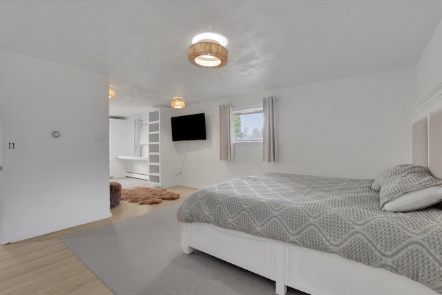 bedroom with light wood-type flooring, baseboards, and a baseboard heating unit