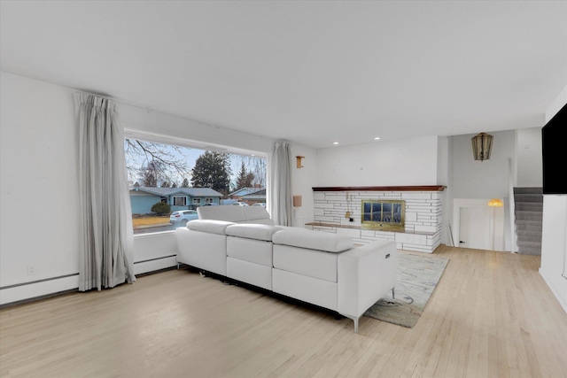 living area featuring light wood-type flooring, a baseboard heating unit, a glass covered fireplace, recessed lighting, and stairway