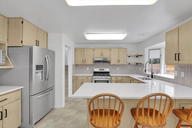 kitchen with tasteful backsplash, under cabinet range hood, light brown cabinetry, stainless steel appliances, and a sink