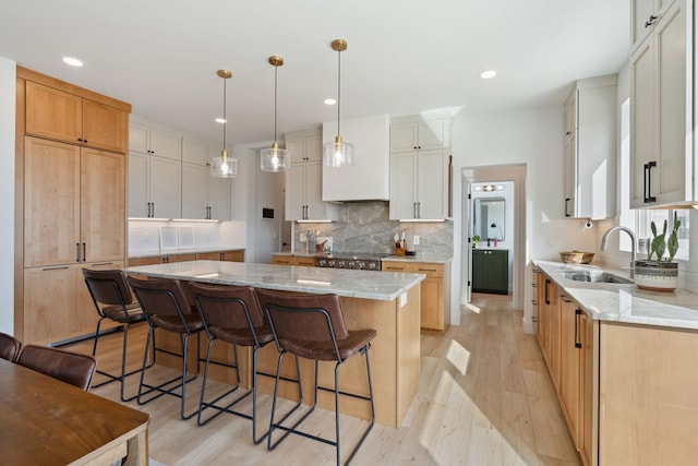 kitchen with light stone counters, a kitchen island, a sink, a kitchen bar, and light wood-type flooring