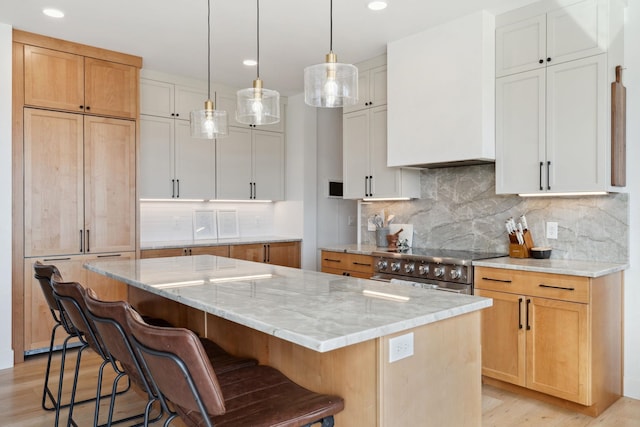 kitchen with stainless steel electric stove, light wood-type flooring, light stone countertops, and a kitchen island