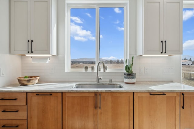 kitchen featuring a sink, light stone counters, backsplash, and white cabinetry