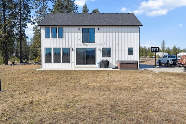 rear view of property featuring a lawn, board and batten siding, roof with shingles, and a hot tub