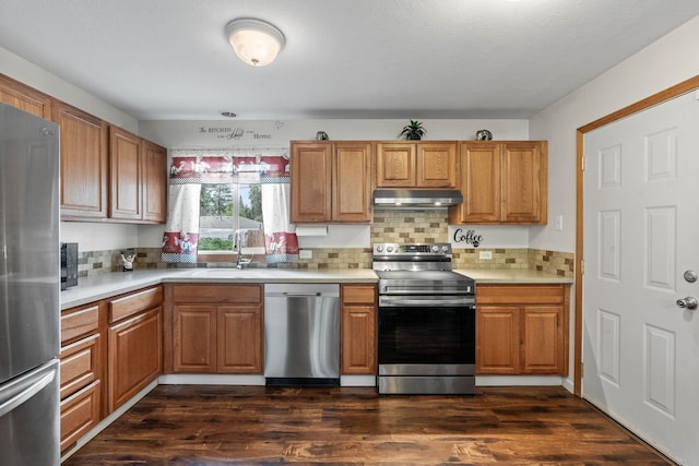 kitchen with under cabinet range hood, dark wood finished floors, light countertops, stainless steel appliances, and a sink