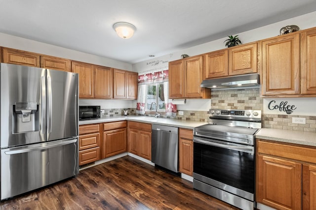 kitchen with a sink, stainless steel appliances, dark wood-type flooring, light countertops, and under cabinet range hood