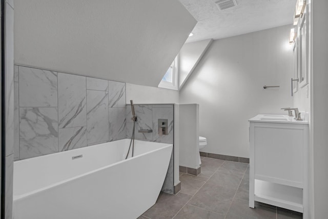 full bathroom featuring visible vents, toilet, vanity, a freestanding tub, and a textured ceiling