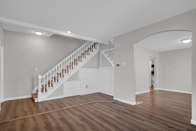 interior space with stairway, arched walkways, a textured ceiling, and wood finished floors