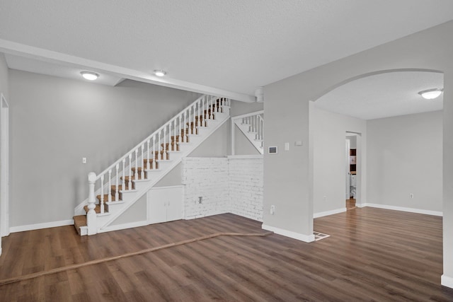 2523 N Nevada St, Spokane, WA 99207 - unfurnished living room featuring a textured ceiling, arched walkways, wood finished floors, stairway, and baseboards