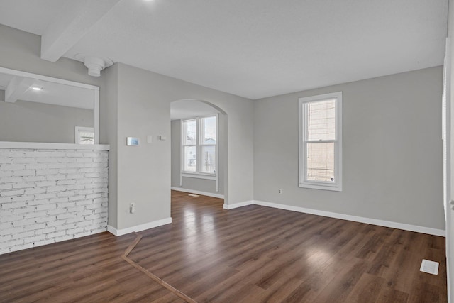 spare room featuring baseboards, arched walkways, plenty of natural light, and wood finished floors