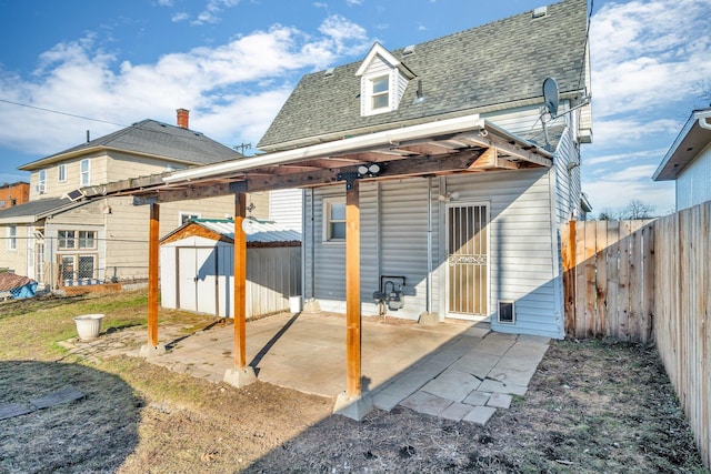 rear view of house featuring roof with shingles, a fenced backyard, an outdoor structure, a patio area, and a storage unit