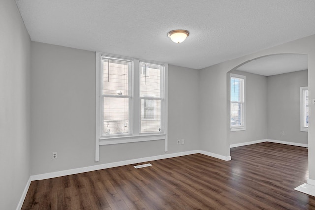 empty room featuring visible vents, dark wood-type flooring, a textured ceiling, arched walkways, and baseboards