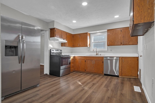 kitchen with visible vents, brown cabinets, under cabinet range hood, a sink, and appliances with stainless steel finishes