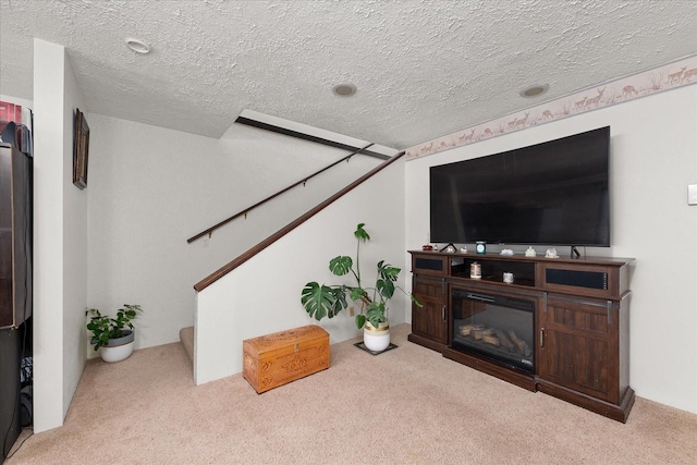 carpeted living area with a glass covered fireplace, a textured ceiling, and stairs