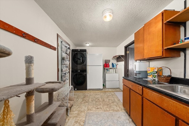 kitchen with open shelves, brown cabinetry, stacked washer / drying machine, and freestanding refrigerator