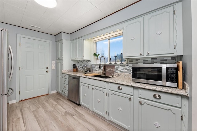 kitchen with light wood-type flooring, visible vents, a sink, backsplash, and stainless steel appliances