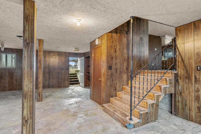 below grade area featuring stairs, wooden walls, a healthy amount of sunlight, and a textured ceiling