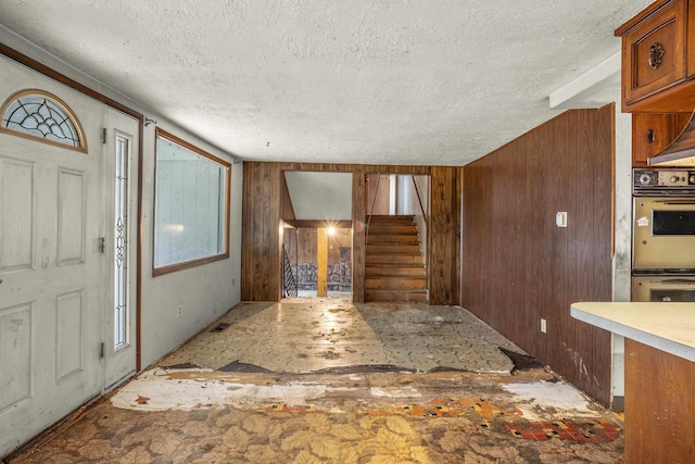 foyer featuring stairway, wood walls, and a textured ceiling