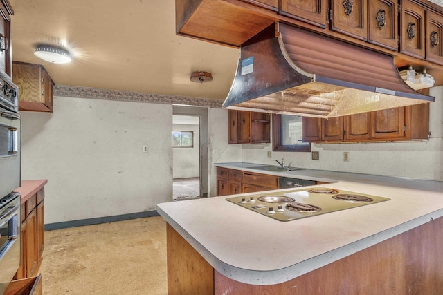 kitchen with brown cabinetry, custom exhaust hood, a peninsula, a sink, and electric stovetop