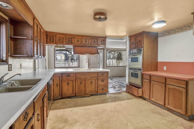 kitchen with multiple ovens, a sink, a peninsula, brown cabinetry, and white cooktop