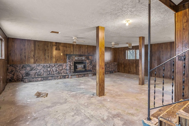 below grade area featuring a fireplace, a textured ceiling, wood walls, and a ceiling fan