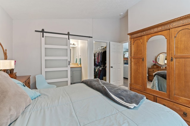 bedroom featuring a walk in closet, lofted ceiling, a barn door, a closet, and ensuite bath