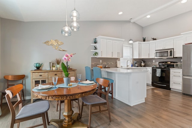 kitchen featuring lofted ceiling, decorative backsplash, appliances with stainless steel finishes, a peninsula, and wood finished floors