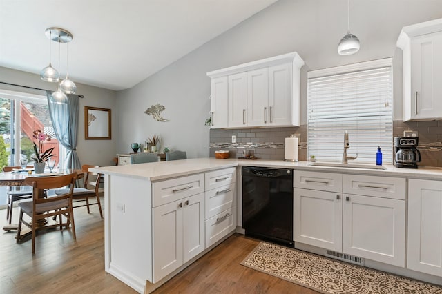 kitchen with a sink, black dishwasher, a peninsula, light countertops, and vaulted ceiling