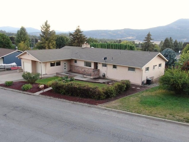 single story home featuring central AC, a front lawn, concrete driveway, a garage, and a mountain view