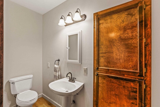 half bathroom featuring toilet, wood finished floors, baseboards, and a sink