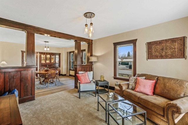 carpeted living area featuring baseboards, a notable chandelier, wood finished floors, and ornate columns