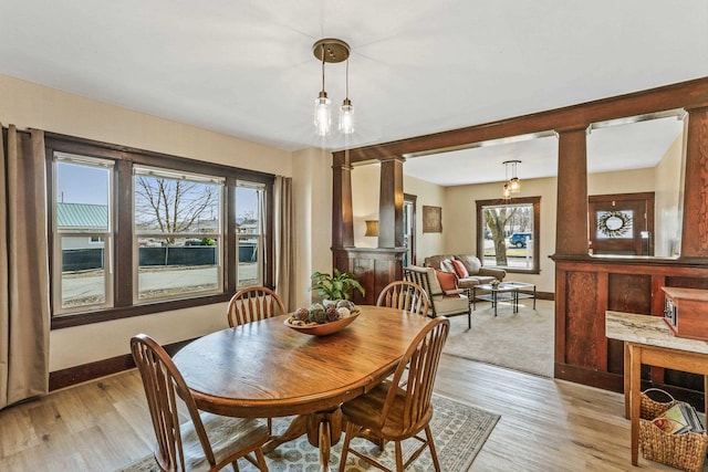 dining space with decorative columns, baseboards, and light wood finished floors