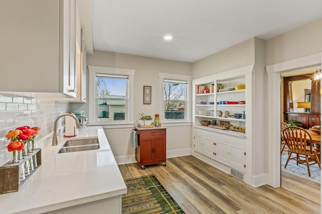 interior space featuring baseboards, light wood-style flooring, a sink, decorative backsplash, and light countertops