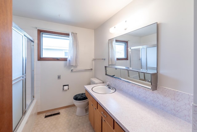 full bath with vanity, visible vents, baseboards, shower / bath combination with glass door, and toilet