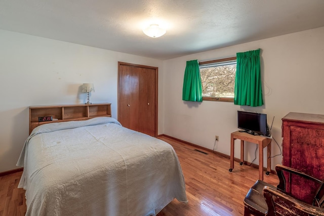 bedroom with wood finished floors, visible vents, a closet, and baseboards