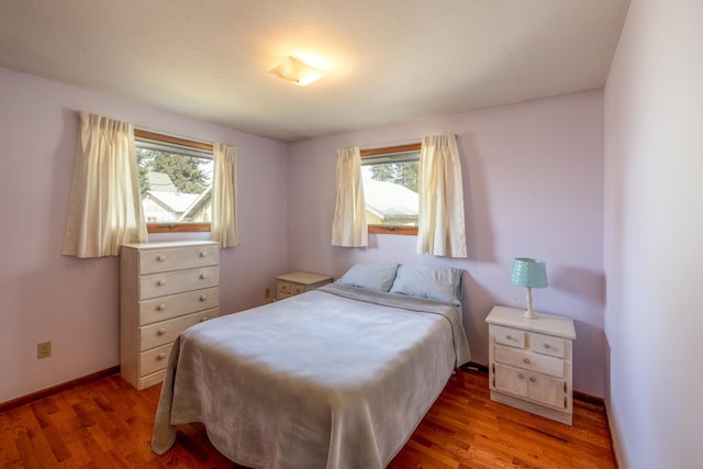 bedroom with multiple windows, wood finished floors, and baseboards