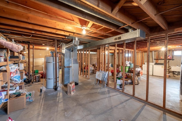 below grade area featuring heating unit, visible vents, water heater, and washer and clothes dryer