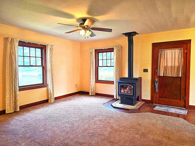 460 E Columbia Ave, Colville, WA 99114 - unfurnished living room featuring a ceiling fan, a wood stove, carpet flooring, baseboards, and a textured ceiling