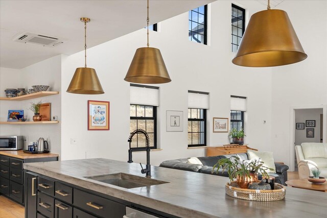 kitchen featuring stainless steel microwave, open floor plan, dark cabinetry, hanging light fixtures, and a sink