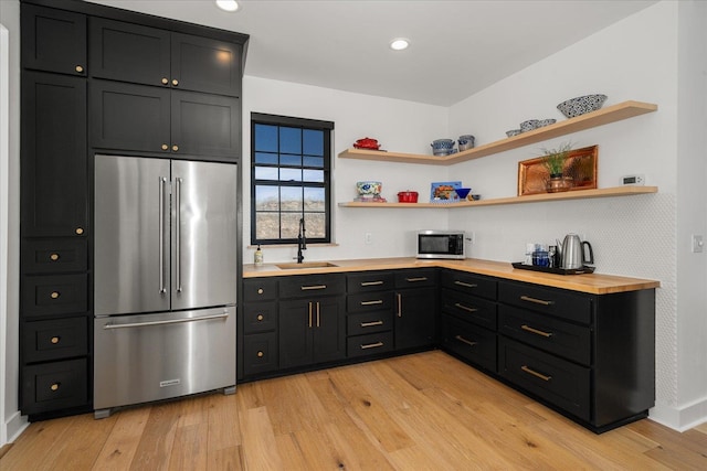 kitchen with light wood-style flooring, high quality fridge, dark cabinetry, and a sink